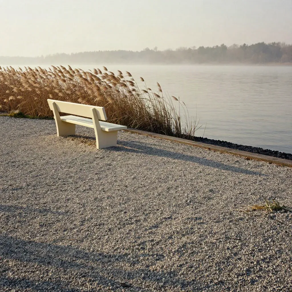 Pale Bank an einem Kiesufer, Schilf im Wind und ruhiges Wasser im Abendlicht.